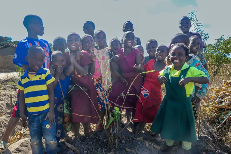 A group of African children all smile and laugh at the camera, they are stood closely together with their arms around eachother